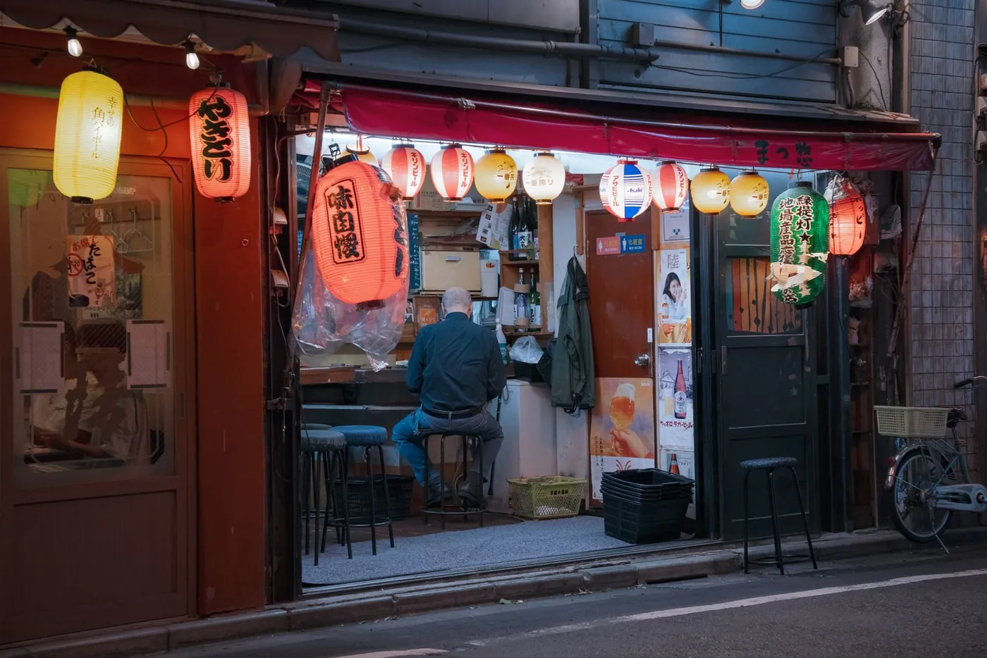 提灯の下がる店先とカウンターに座るひとりの客